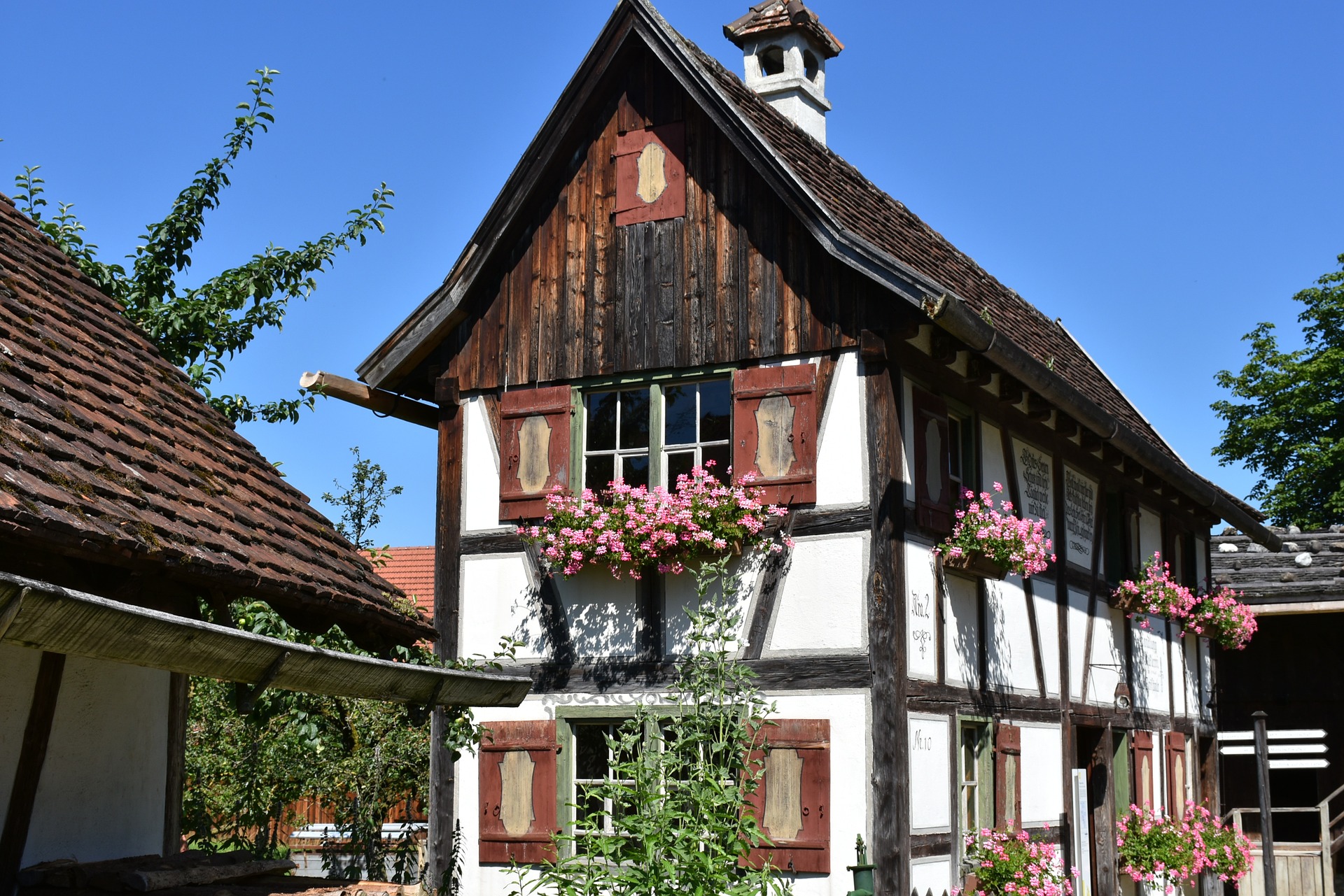 Ein traditionelles Fachwerkhaus mit roten Blumenkästen und blauem Himmel im Hintergrund.